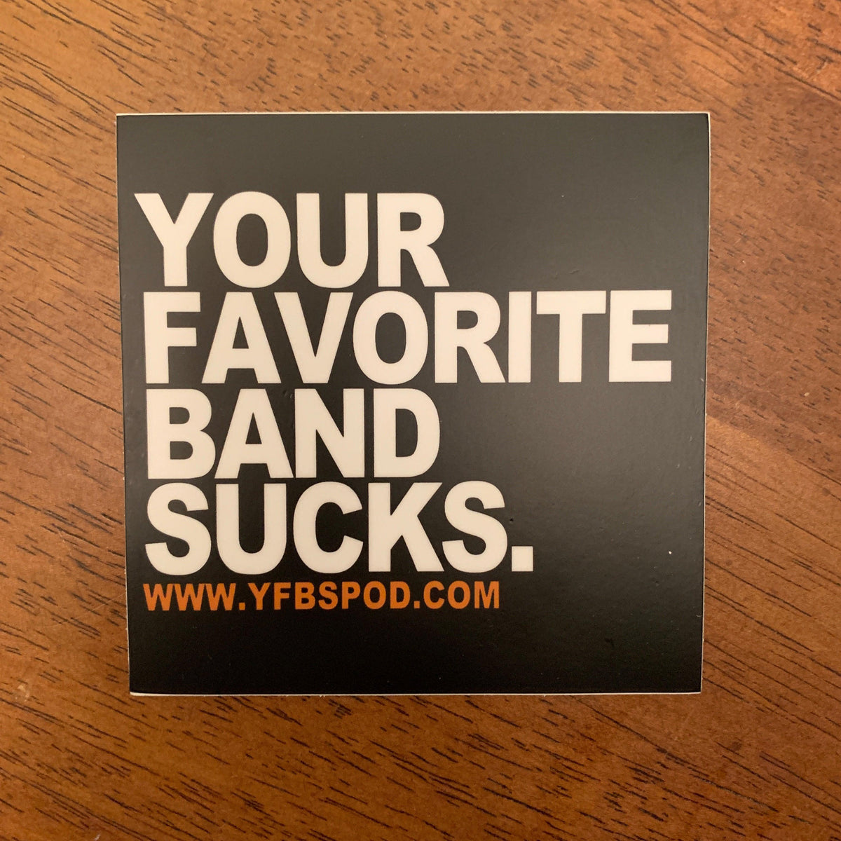 Your Favorite Band Sucks Sticker on a wood surface, black vinyl sticker with white lettering